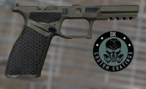 Close-up of a camouflage-green pistol grip and slide with a hex-pattern textured grip and a round DK Custom Coatings patch overlapped on the right side.